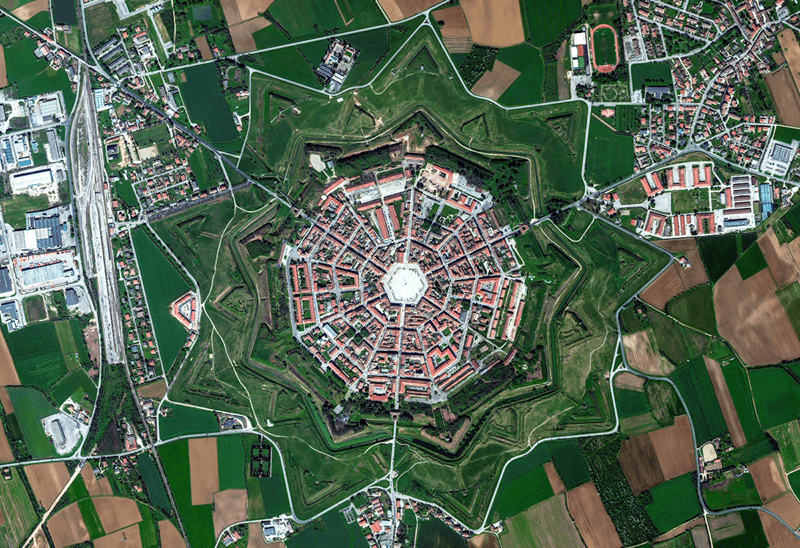 Aerial view of a star-shaped fortress city surrounded by fields and roads, with concentric rings of buildings and green spaces.