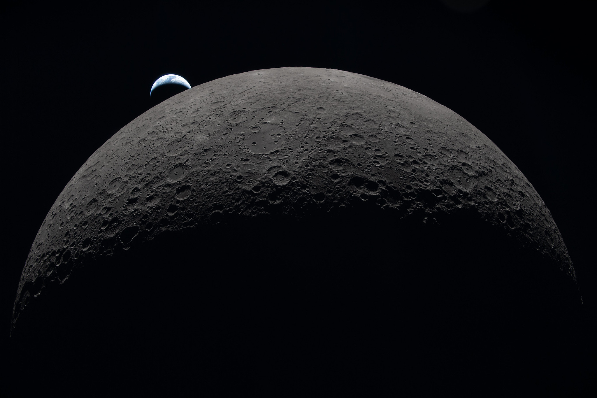 A view of Earth's partially illuminated crescent rising over the Moon&rsquo;s heavily cratered surface, capturing the blackness beyond during Artemis II's distance record.