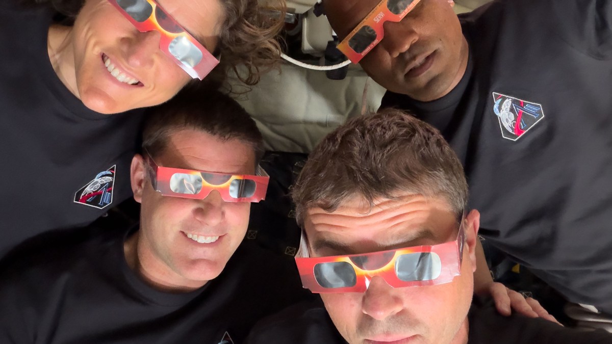 Four people wearing black shirts and eclipse glasses look up at the camera indoors, their excitement echoing the spirit of the Artemis II distance record mission.