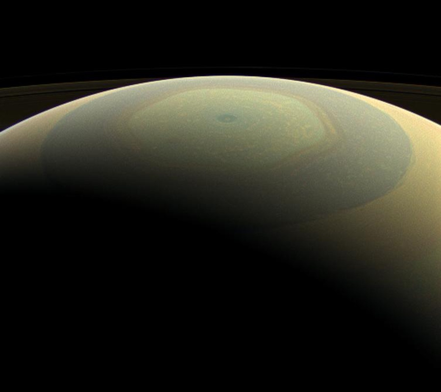 View of Saturn's north pole displaying a distinct hexagonal storm pattern, with the planet's curved horizon visible at the top.