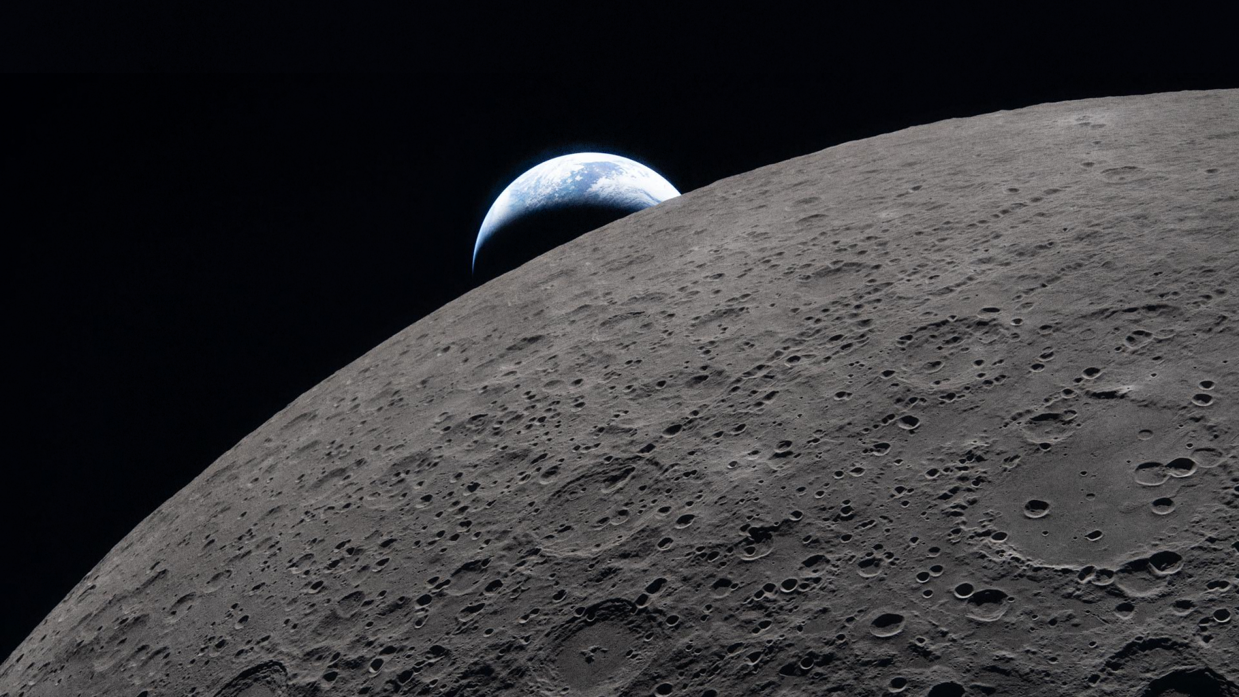 The Earth appears above the horizon of the moon, with the lunar surface in the foreground and space in the background.