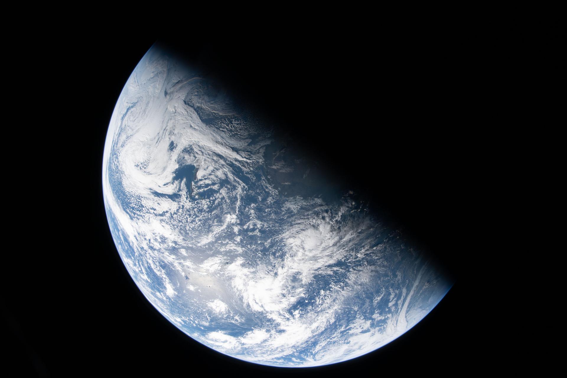 A view of Earth from space, partially illuminated, shows blue oceans, white clouds, and a shadow covering part of the planet&mdash;a perspective reminiscent of Artemis II&rsquo;s journey and the hope it inspires for our moon and Earth.