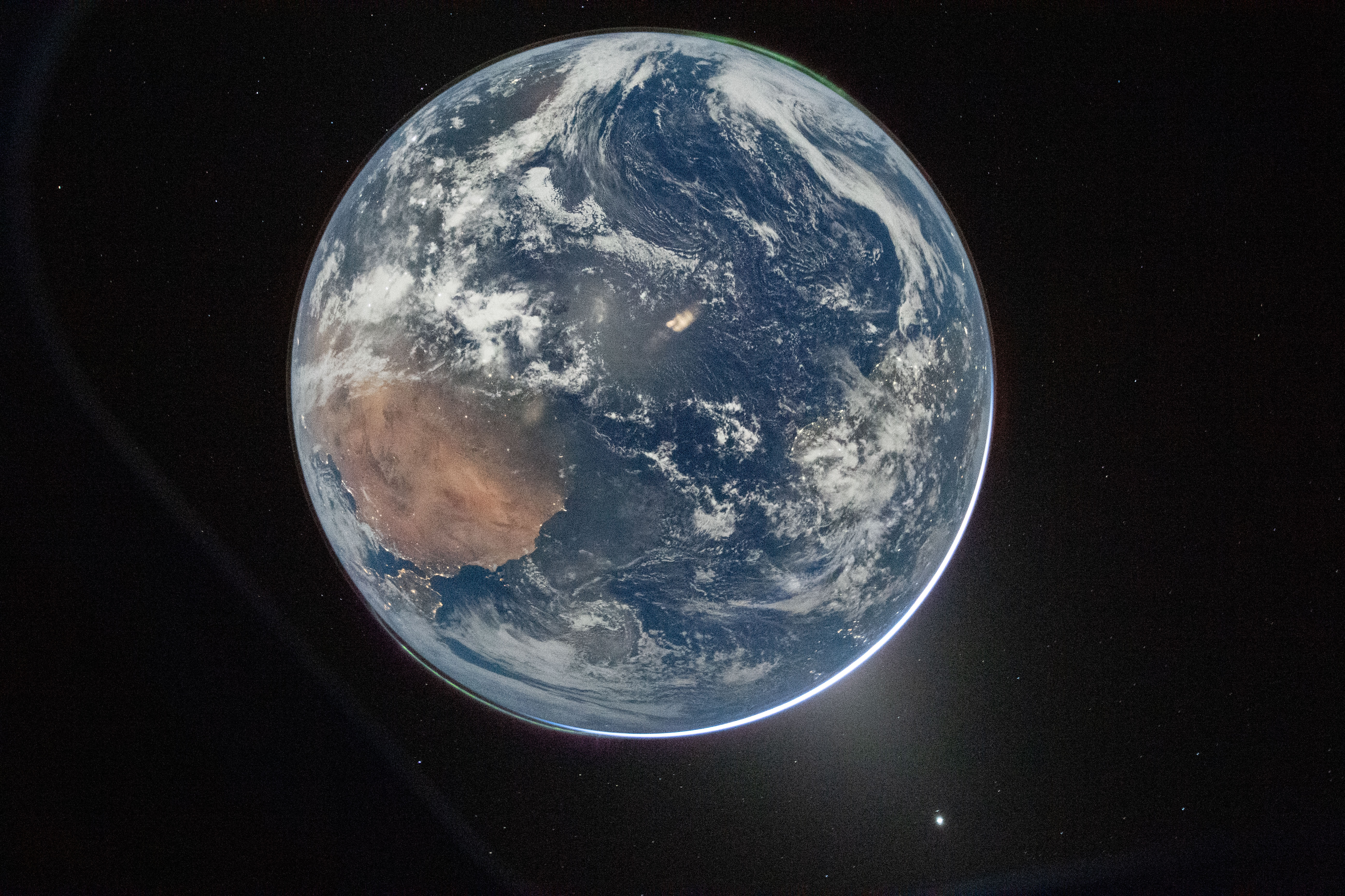 A view of Earth from space showing the continents, oceans, and cloud formations, with a dark background and a small bright object&mdash;possibly the Artemis II moon&mdash;visible below the planet, evoking a sense of hope for exploration.