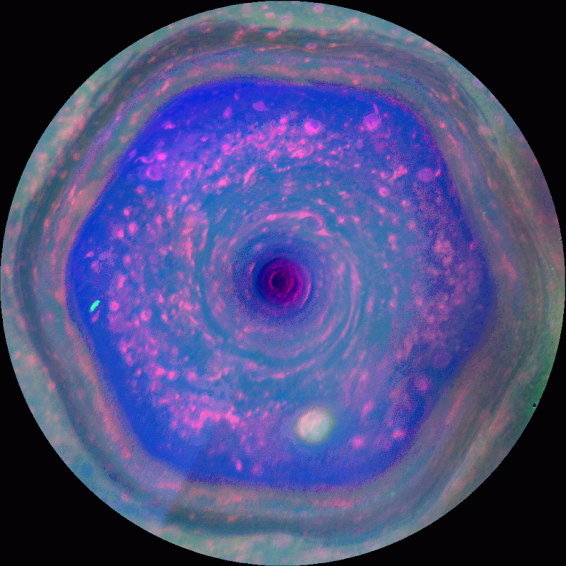 False-color image of Saturn&rsquo;s north polar vortex, featuring a hexagonal storm pattern with swirling clouds in shades of blue, purple, and pink.