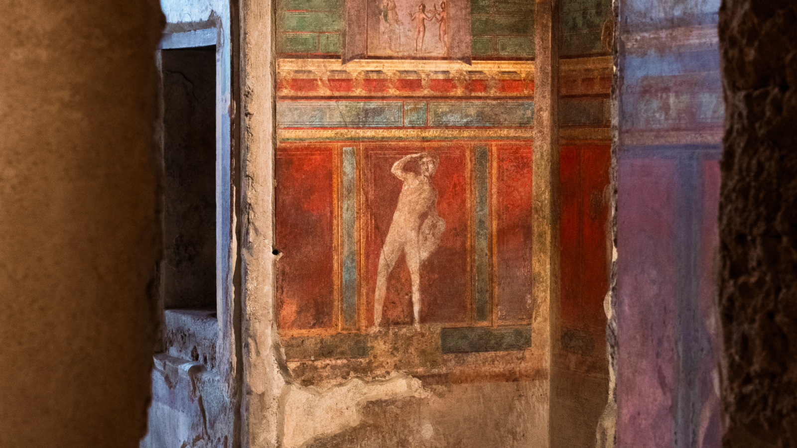 Ancient wall fresco depicting a standing human figure, surrounded by red, green, and brown decorative panels&mdash;an evocative remnant bearing the marks of history&rsquo;s lost voices and the passage of time.