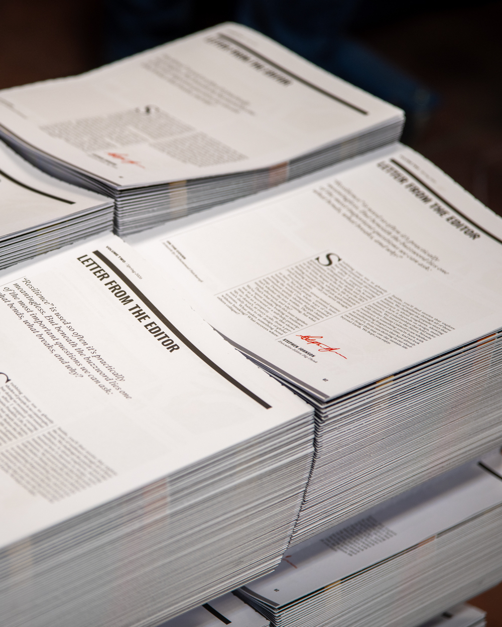 Stacks of printed newsletters or magazines are arranged on a flat surface, each featuring a "Letter from the Editor" section on the front page.